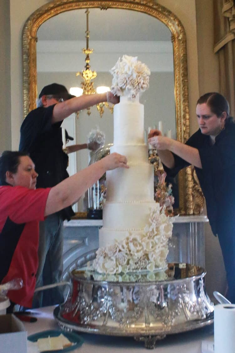3 people working on placing flowers on 9 tier cake 