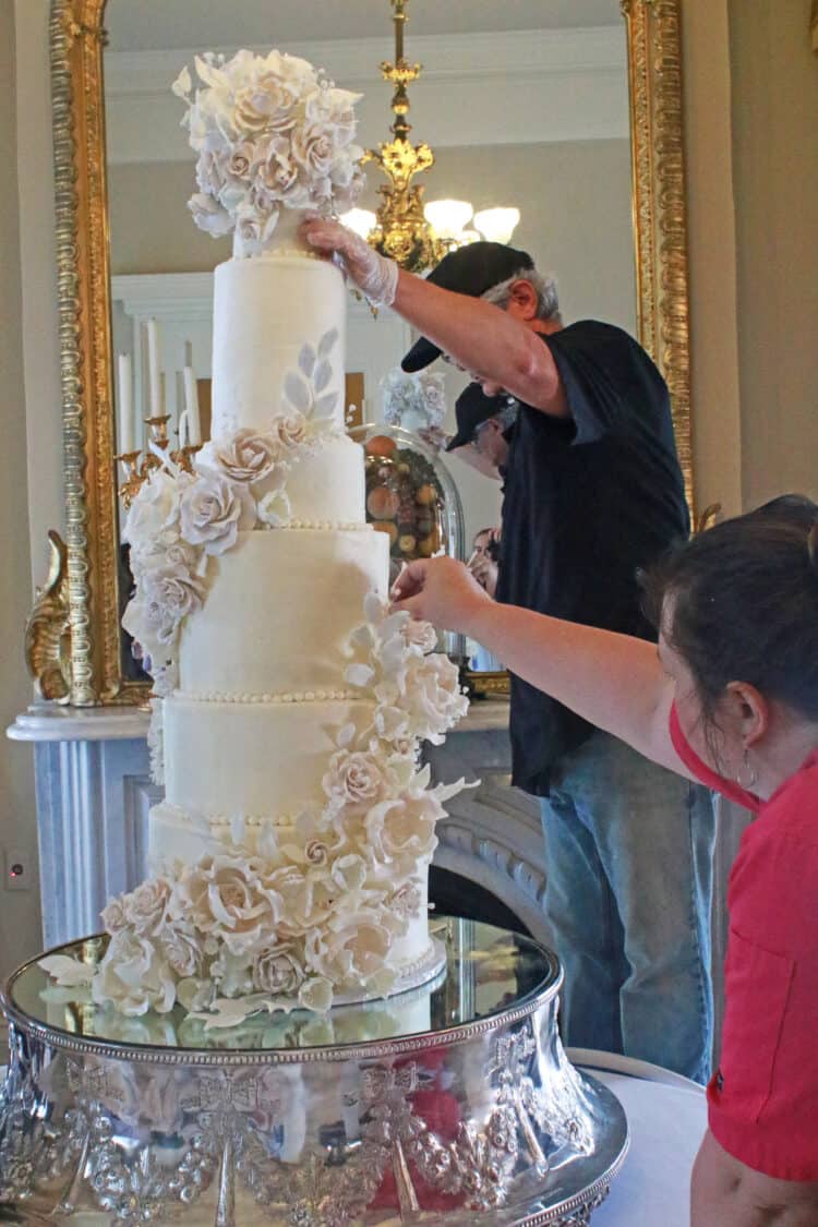 cake being held steady while being assembled by 3 people 
