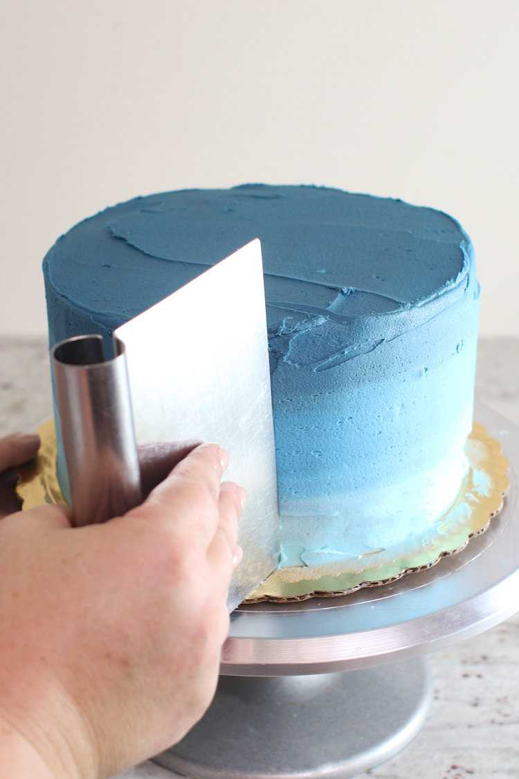 using a bench scraper to smooth blue frosting on a cake on a turntable