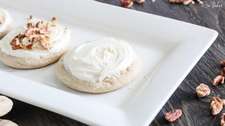White dish with butter pecan cookies with frosting and chopped pecans added on top