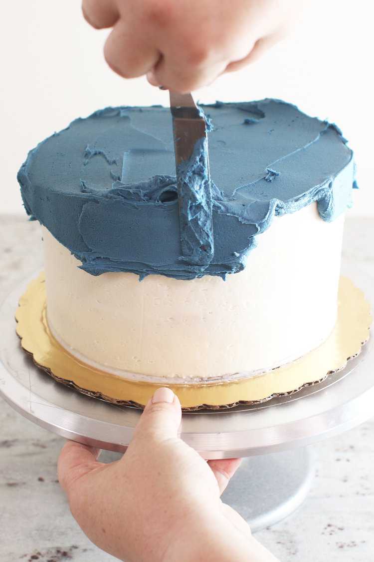 A cake on a cake turntable with blue frosting being spread with an offset spatula - feature photo for the best cake decorating tools