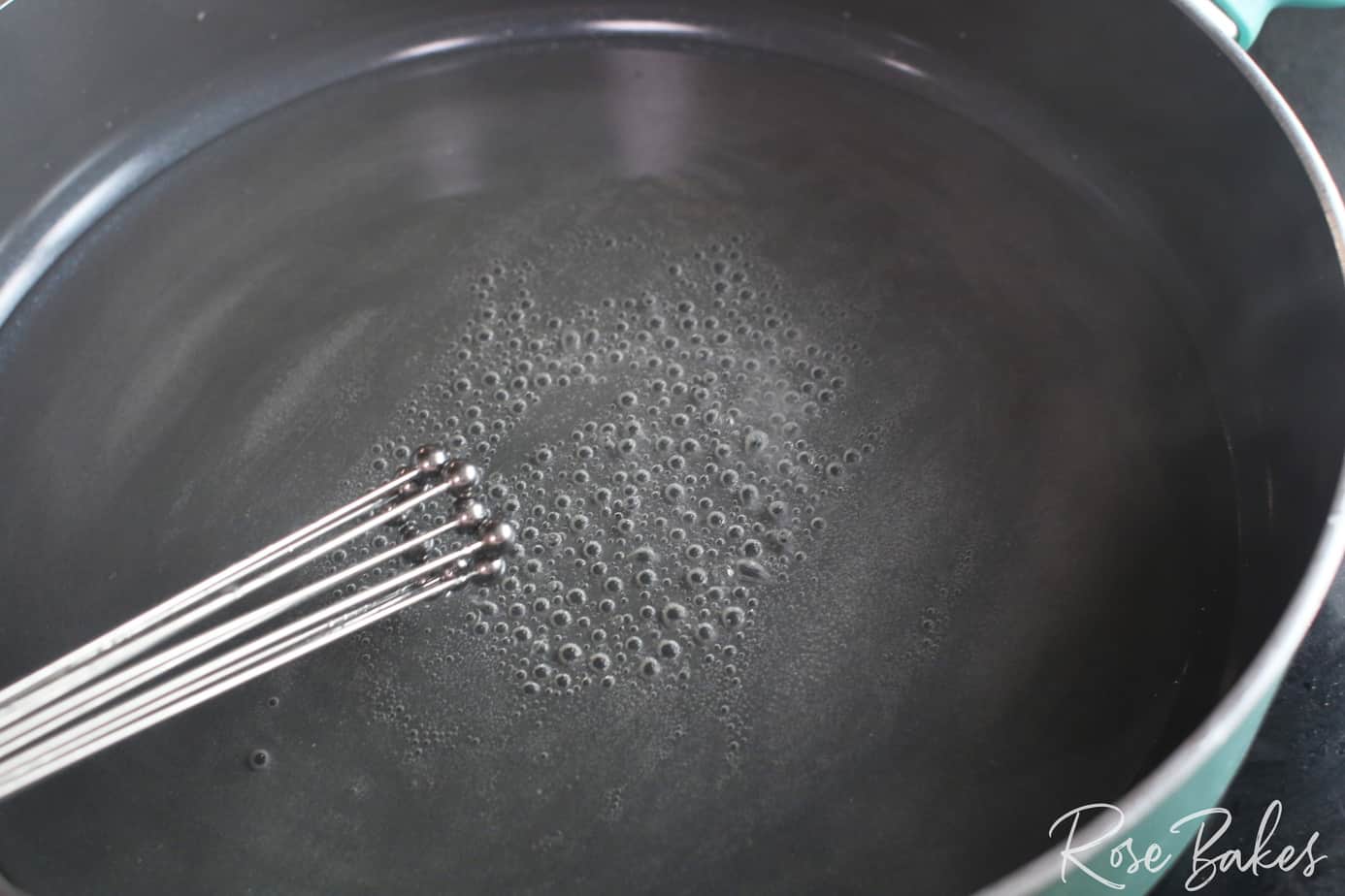 boiling sugar water with whisk in shallow pan