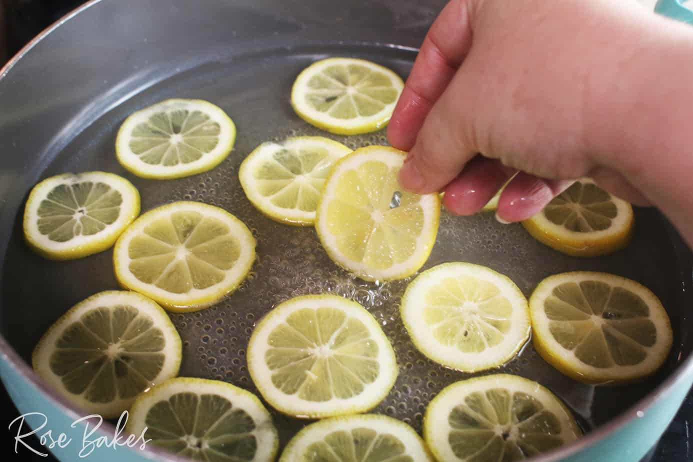 hand placing lemon slices in a shallow pan of sugar water that is boiling