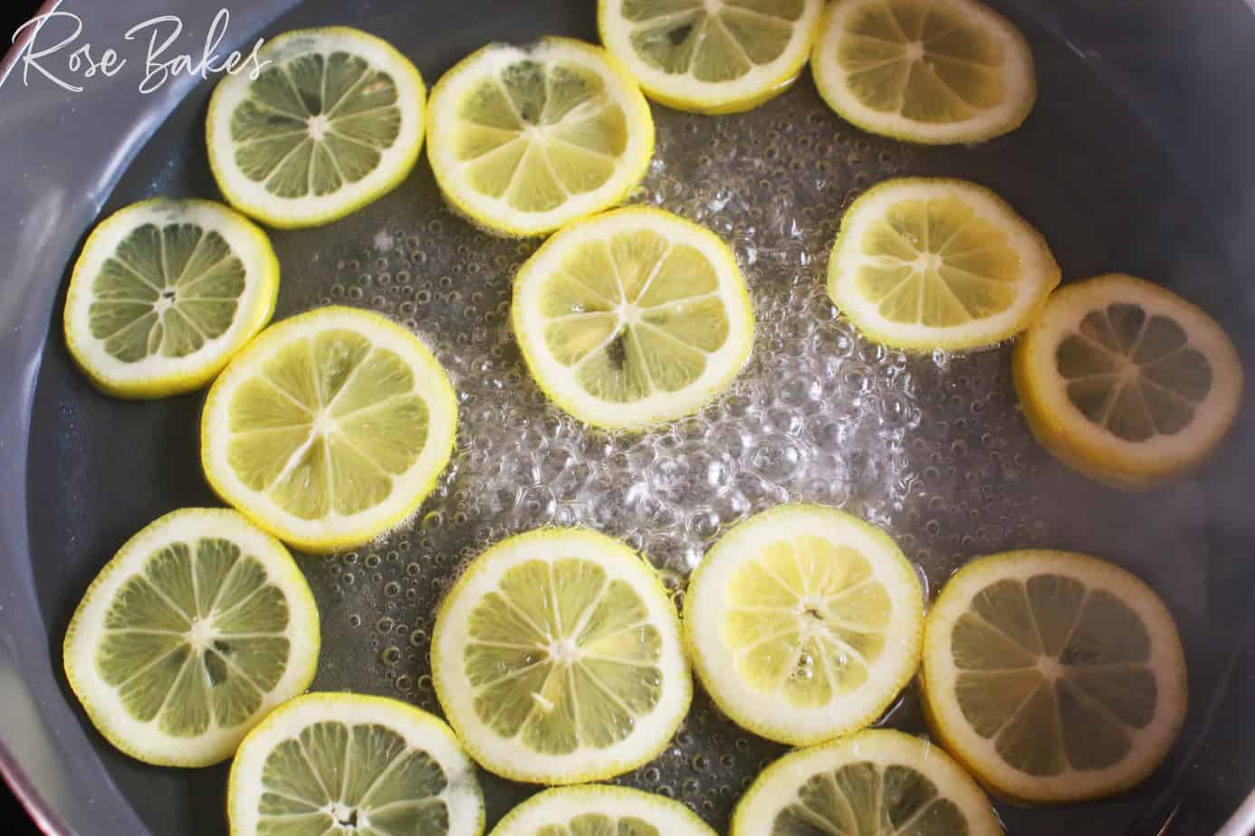lemon slices in a shallow pan of sugar water that is boiling to make candied lemons