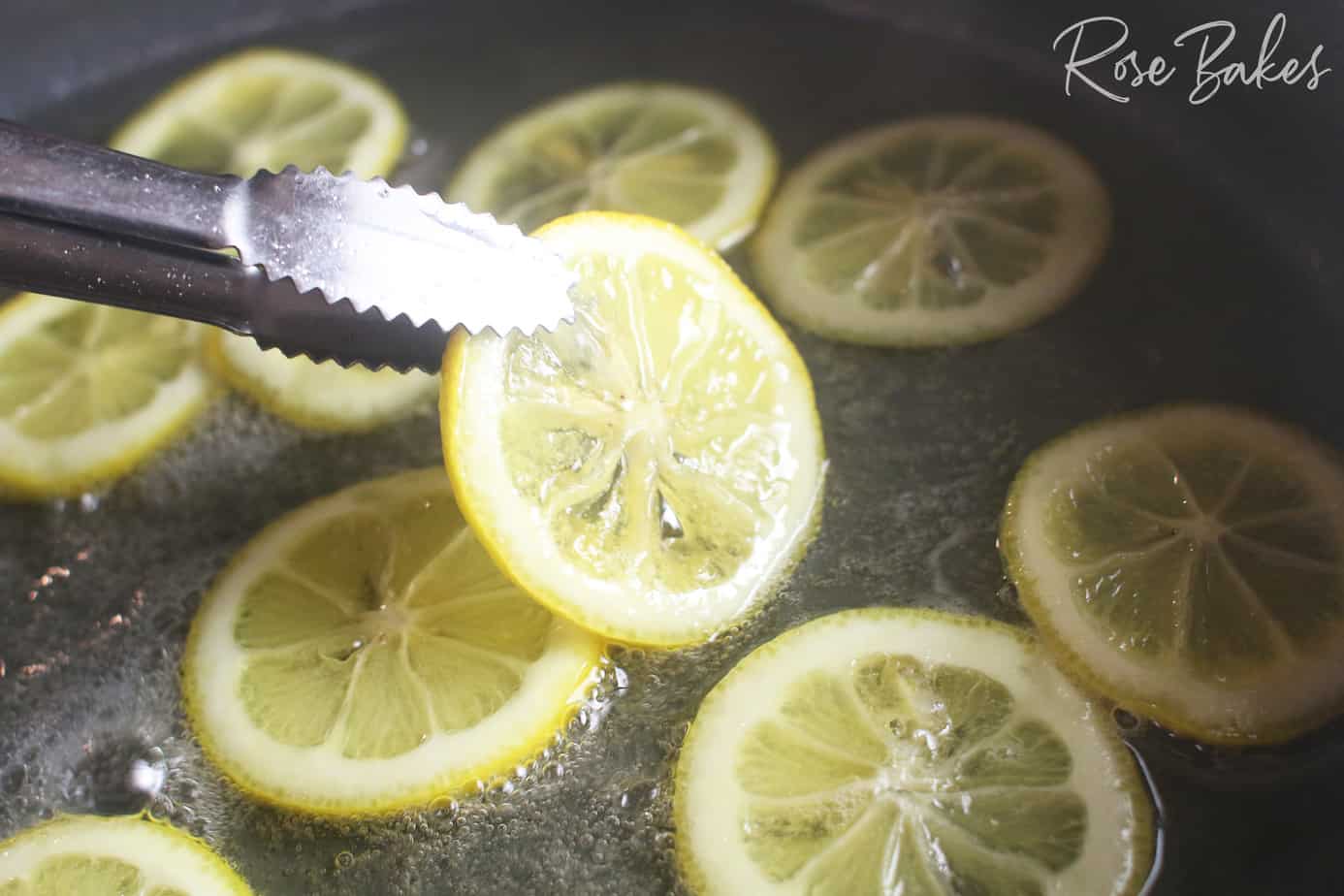 tongs flipping lemon slices in a shallow pan of sugar water that is boiling