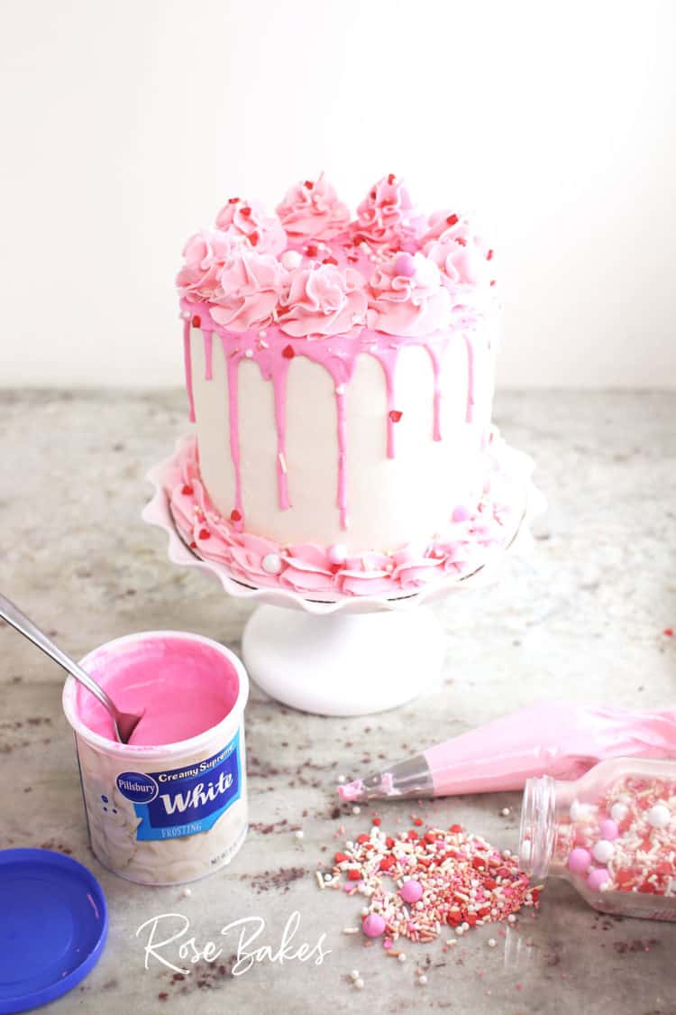 Valentine's pink and white Canned Frosting Drip Cake with a can of colored frosting, sprinkles and a piping bag with pink frosting