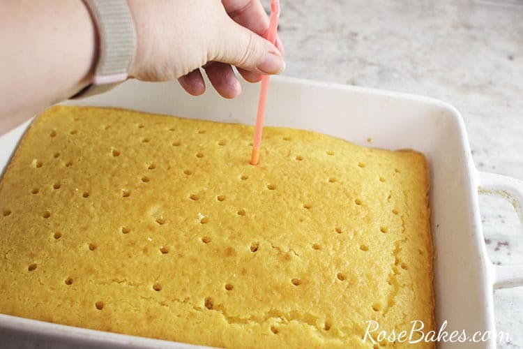 poking holes in a yellow cake with a straw
