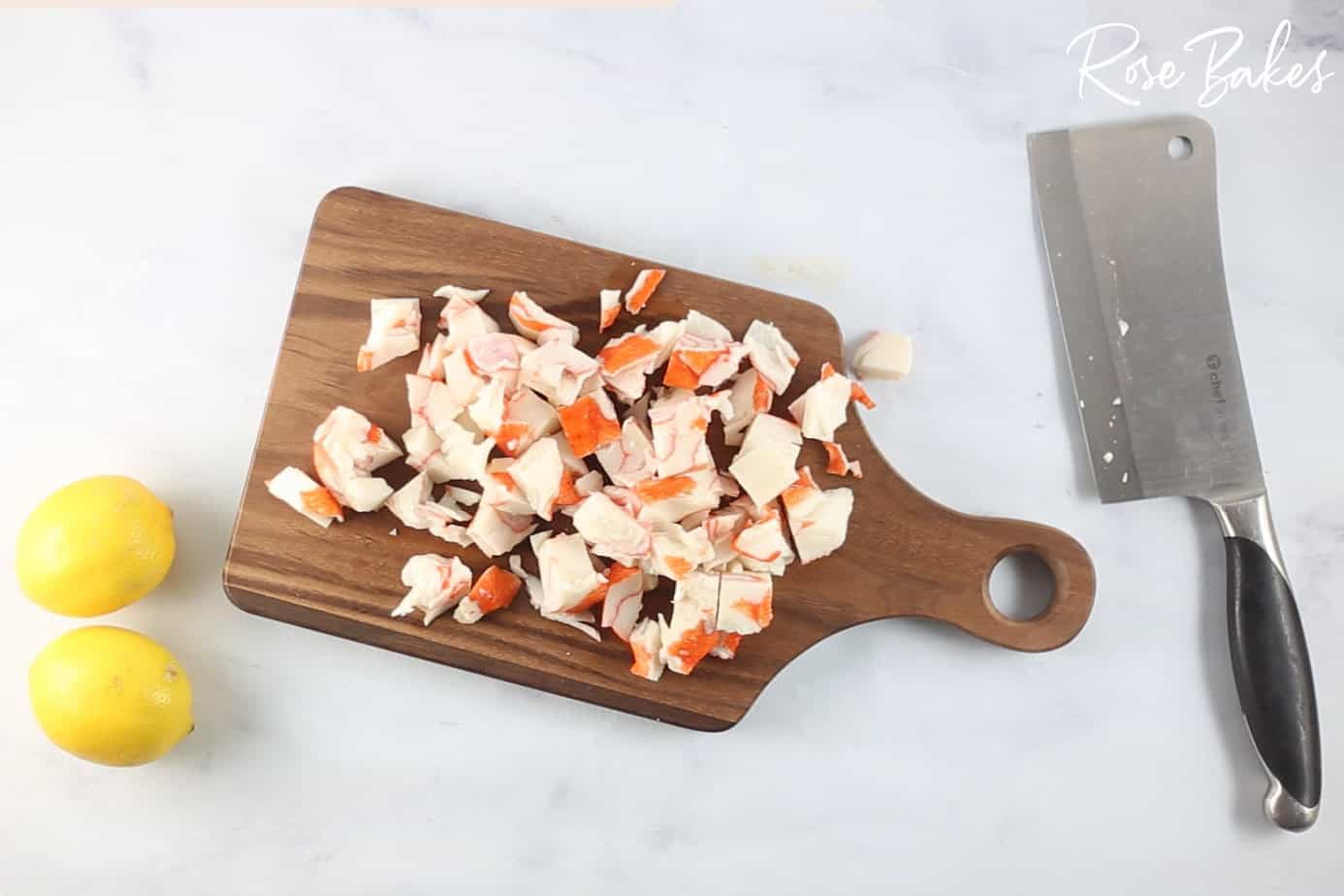 chopped imitation crab meat on a cutting board with lemons and a knife on the counter next to it