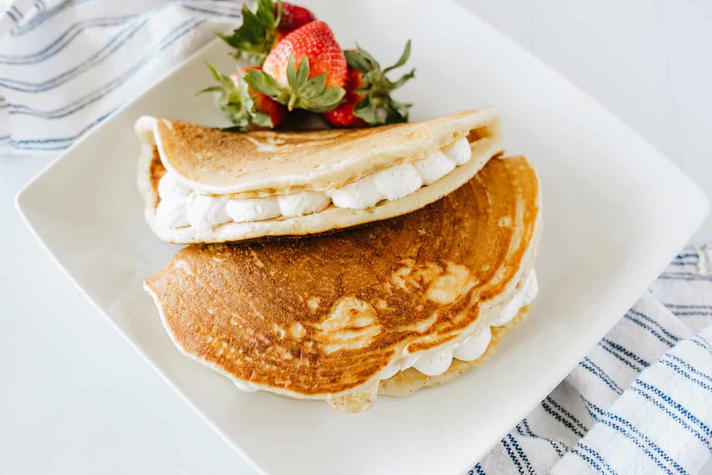 two buttermilk pancakes stuffed with no-bake cheesecake filling folded like tacos on a white plate with fresh strawberries