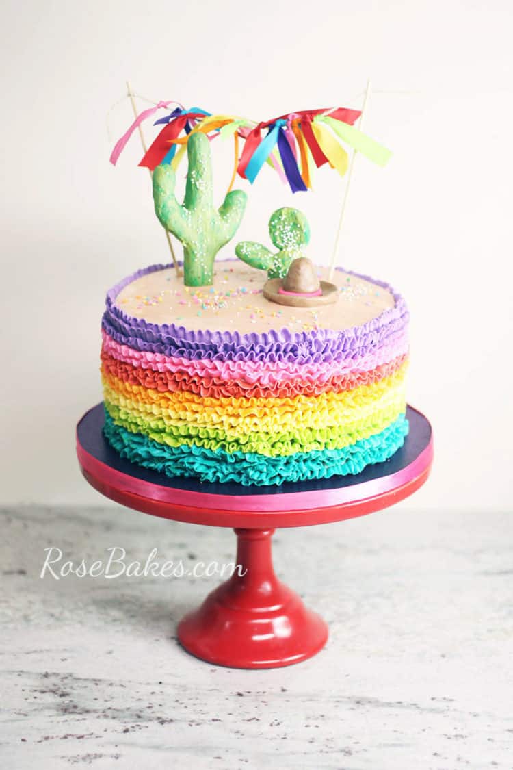 rainbow buttercream ruffles fiesta cake with cactus cake toppers and ribbon bunting on red cake stand