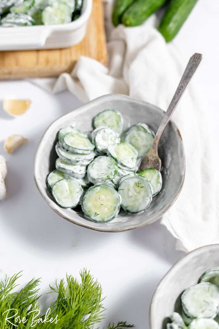 german cucumber salad tossed in a creamy white german dressing in a white bowl with a spoon