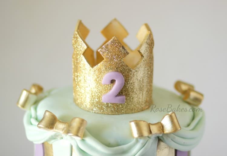 picture of a glittery gold tiara with a purple 2 on the front on top of a cake
