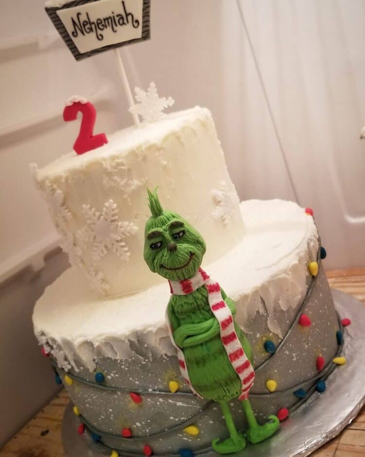 white snowflake cake with grinch character on front with christmas lights by Cake by Sugar Kisses