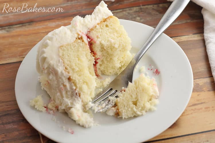 half eaten slice of white cake with raspberry filling and vanilla buttercream on a white plate