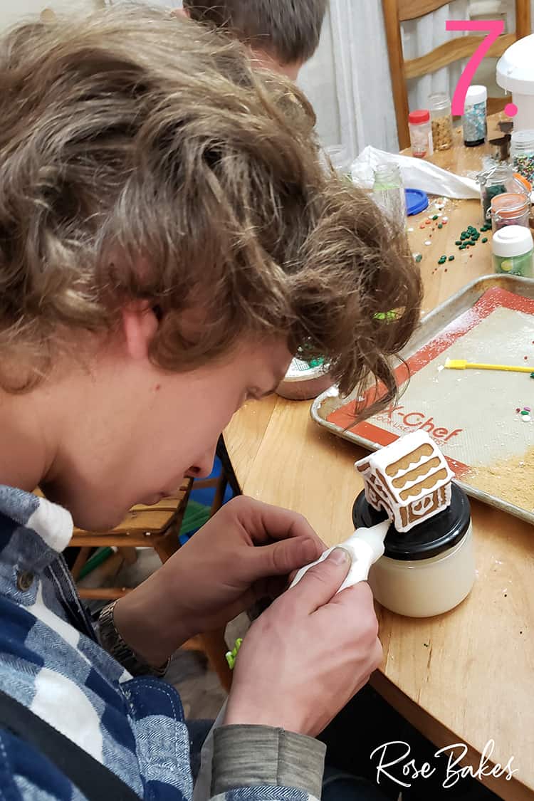 Young man decorating mini gingerbread house with icing