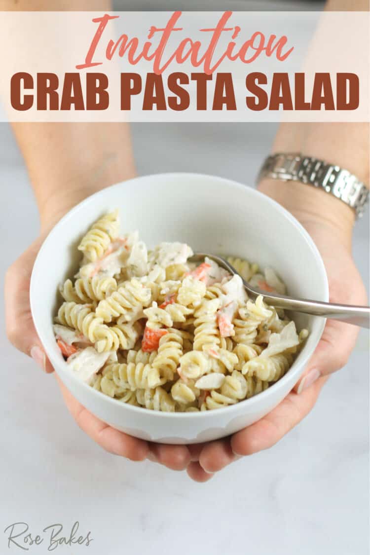 out stretched arms holding the bowl of pasta salad made with rotini. Text at the top of the image reads, "Imitation Crab Pasta Salad"
