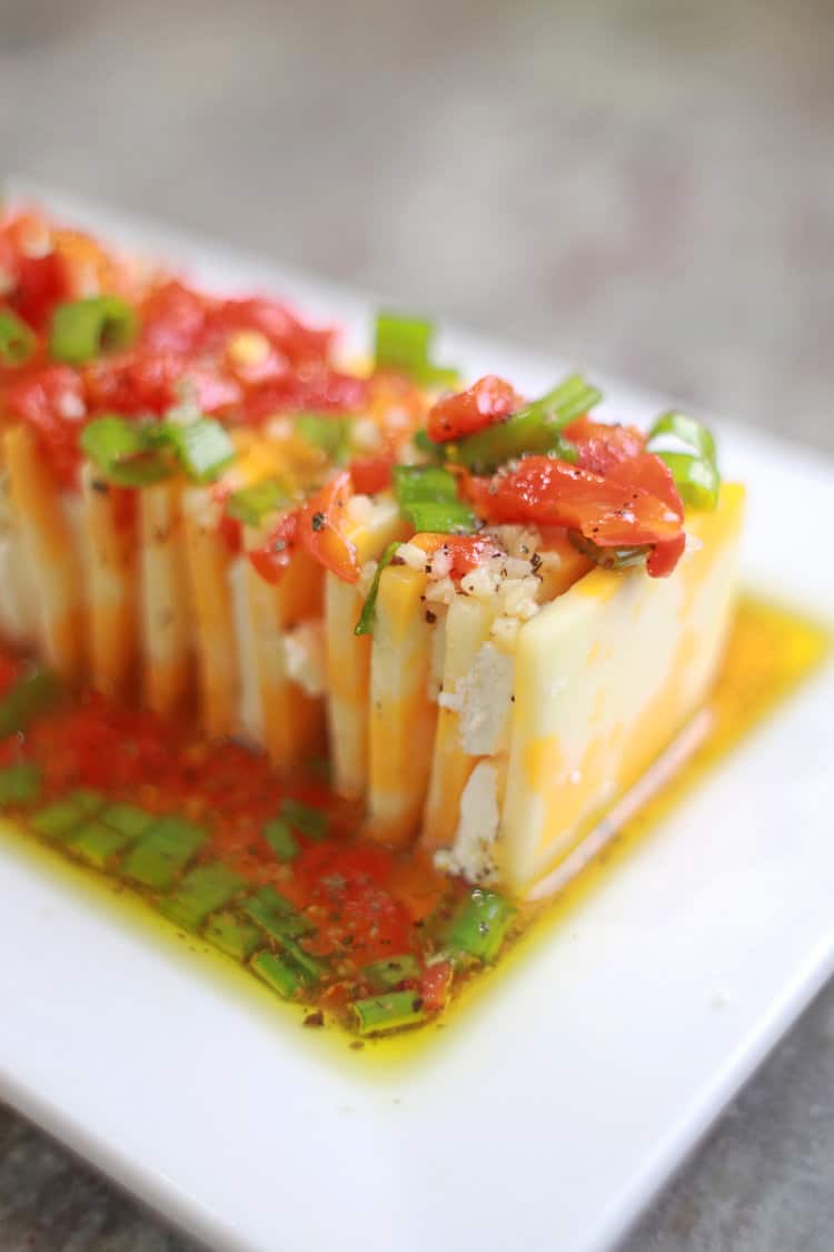Marinated cheese - slices of cheese stacked on a white platter with a marinated poured over the top