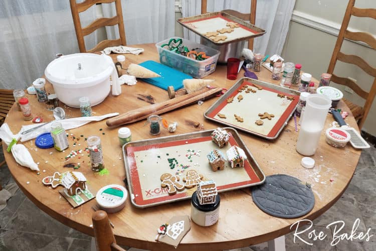 How to Make Mini Gingerbread Houses with Kids post - messy table with all the cookies, houses and supplies scattered