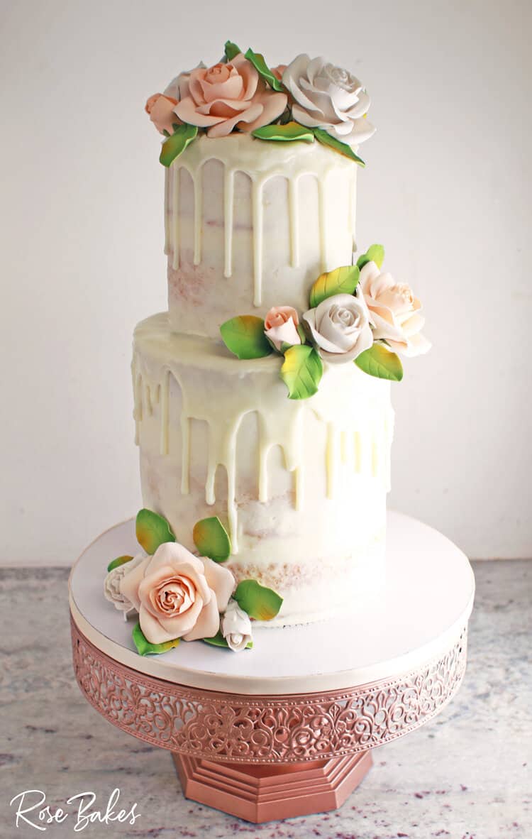 tiered naked cake with white drip plus white and peach colored sugar roses