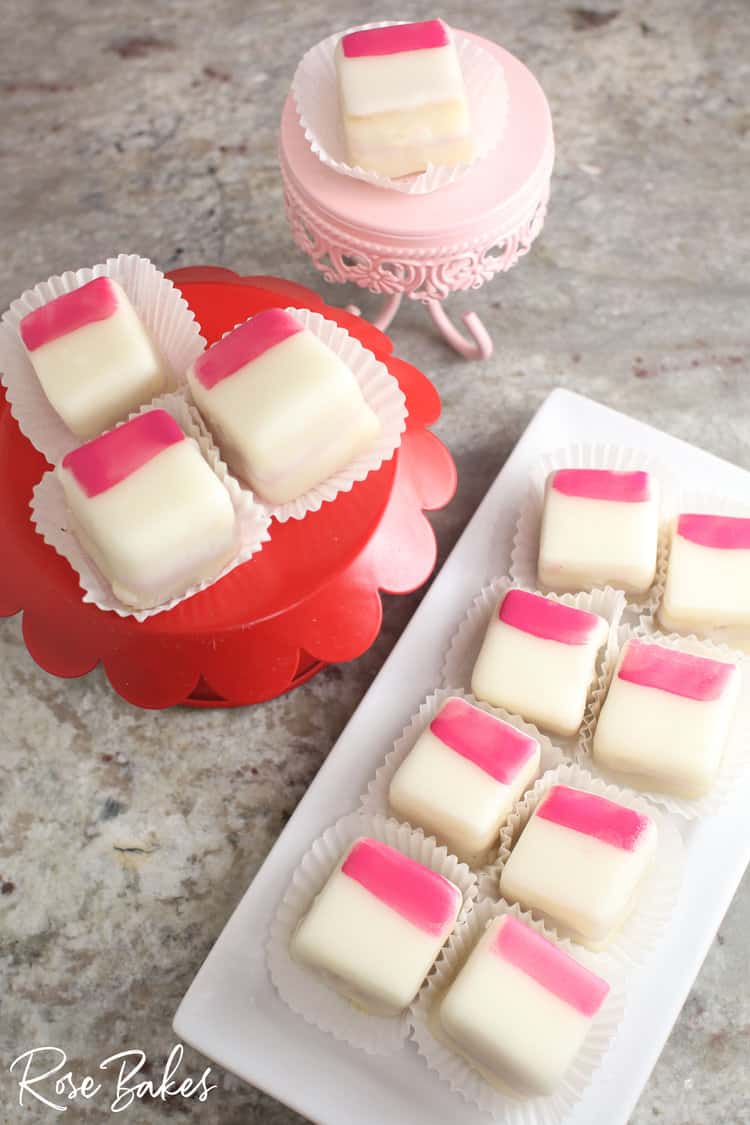 Petit fours with pink brush strokes displayed on cake stands and a platter