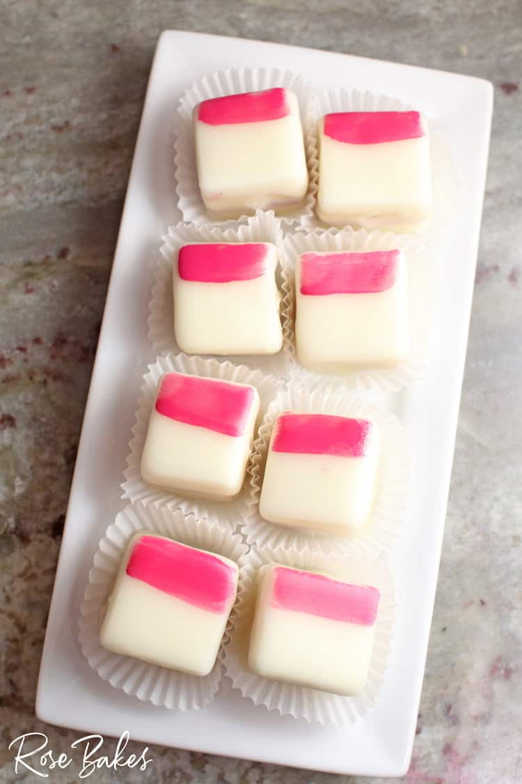 Petit fours with a pink brush stroke on each displayed on a rectangular platter 