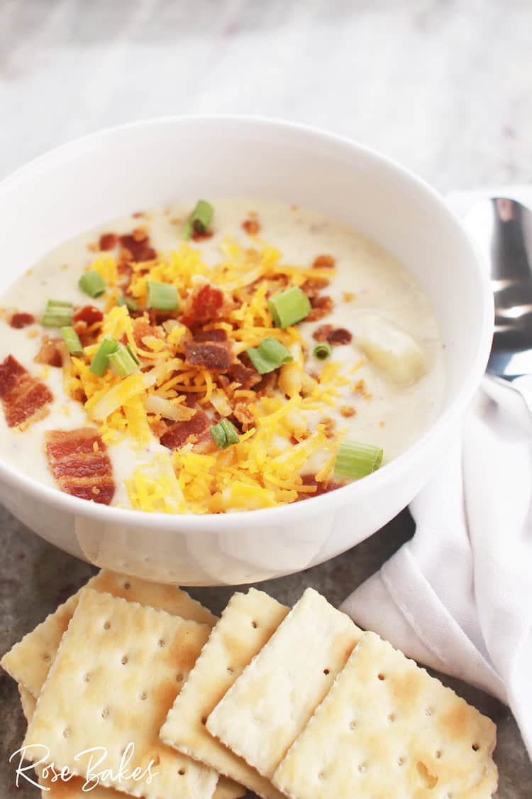 Red potato soup with cream cheese in a bowl with bacon and cheese on top and crackers on the side