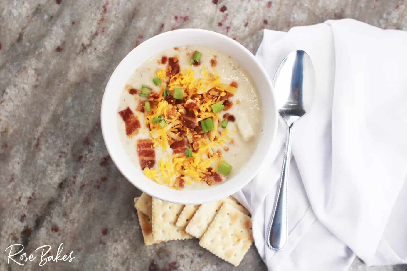 Red potato soup with cream cheese in a bowl with bacon and cheese on top and crackers on the side and a spoon next to the bowl