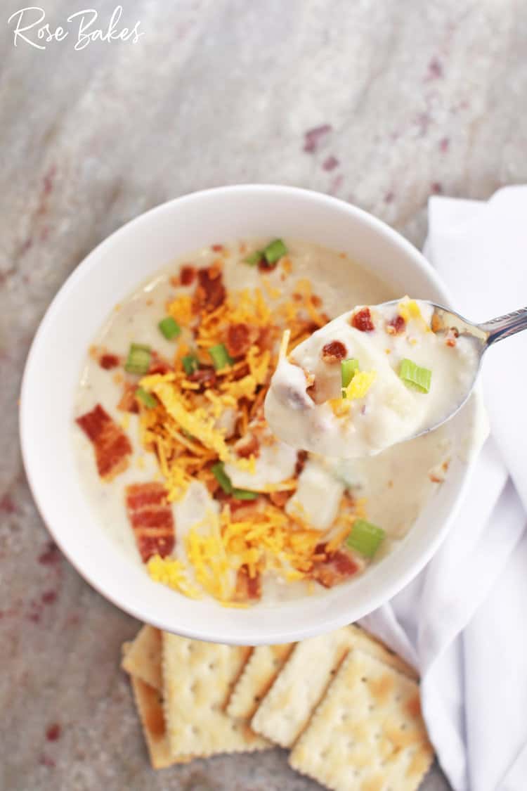 a spoon of red potato soup with cream cheese in a bowl with bacon and cheese on top and crackers on the side