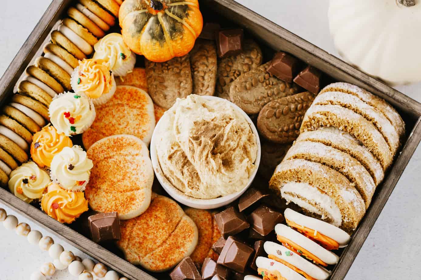 Pumpkin Cream Cheese Dip in a white bowl in the middle of a dessert board filled with cookies and candies
