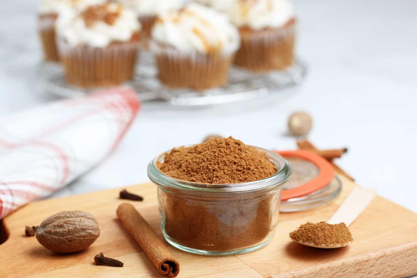 pumpkin pie spice ingredients in a small clear bowl on a cutting board with cupcakes in the background