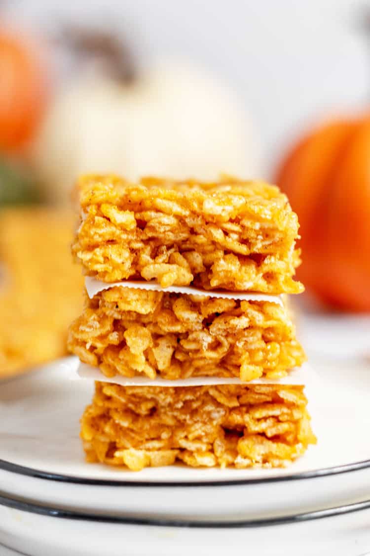 Pumpkin Rice Krispie Treats stacked on a plate with parchment paper between.