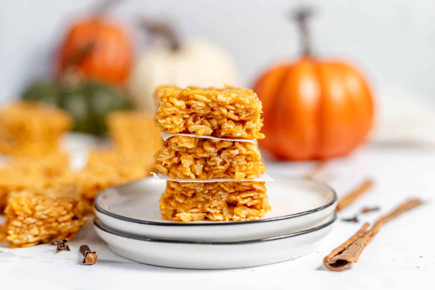 Pumpkin Rice Krispie Treats stacked on a plate with parchment paper between.