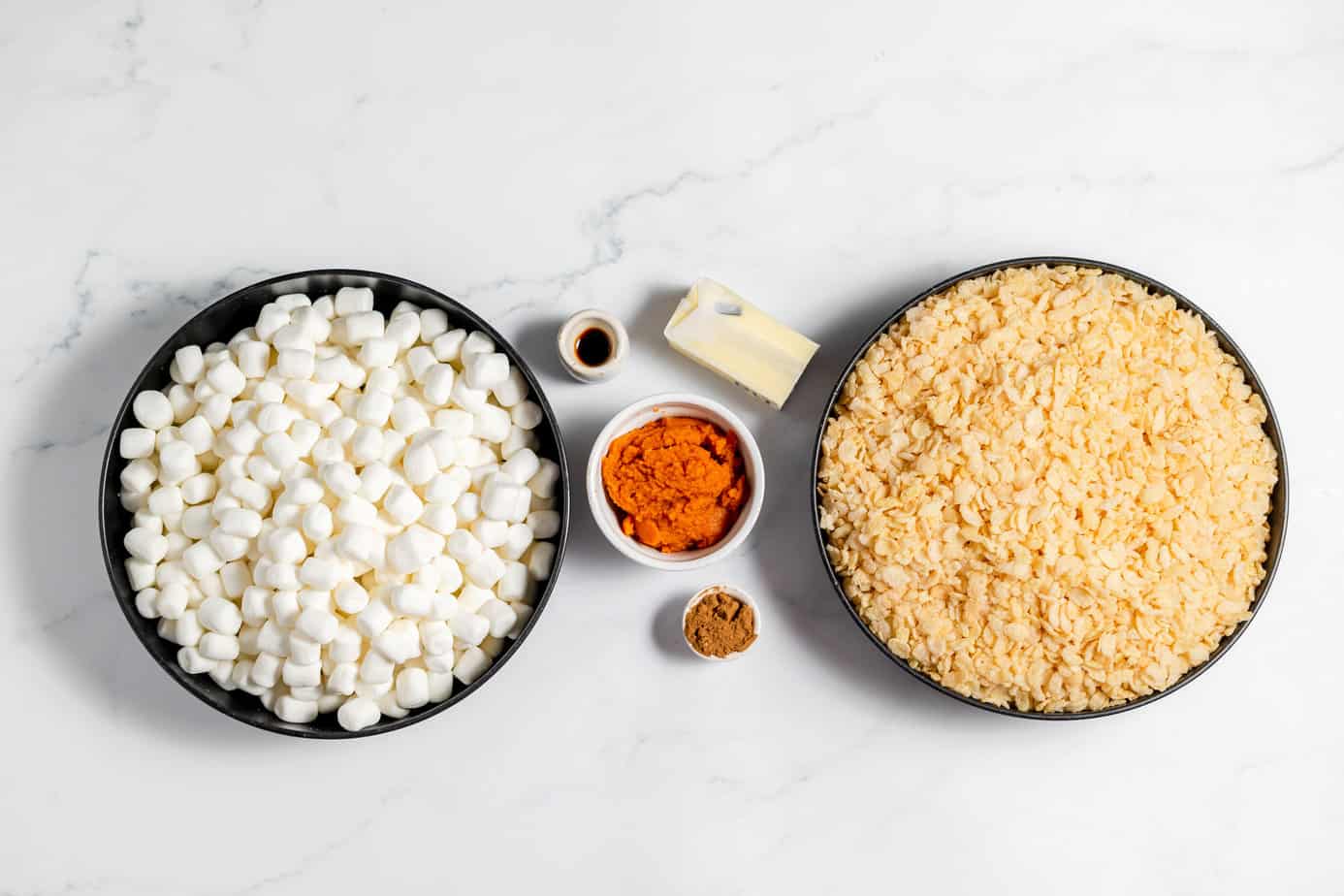 Pumpkin Rice Krispie Treats ingredients in bowls: marshmallows, rice cereal, pumpkin puree, pumpkin pie spice, vanilla and butter