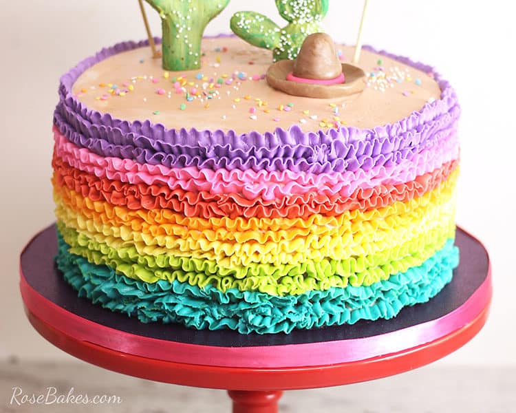 rainbow buttercream ruffles cake on red cake stand with cactus topper for fiesta cake