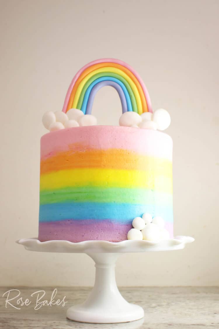 How to Smooth Frost a Cake and How to Get Sharp Buttercream Edges {Video Tutorial} - shown on a smooth-frosted buttercream rainbow cake on a white cake stand with fondant rainbow and clouds topper