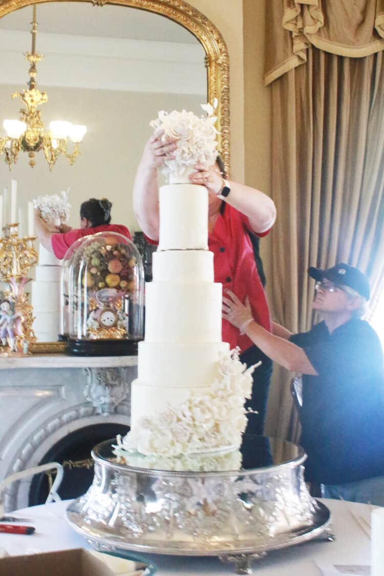 Very top tier being placed on cake by 2 people