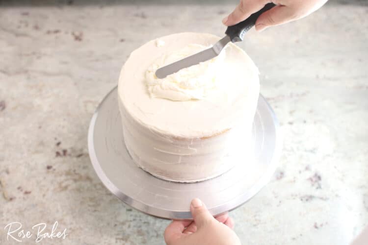 buttercream icing being spread on 1 tier crumb layer cake on cake stand 