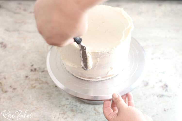 buttercream icing being smoothed on white cake with spatula to create sharp edge