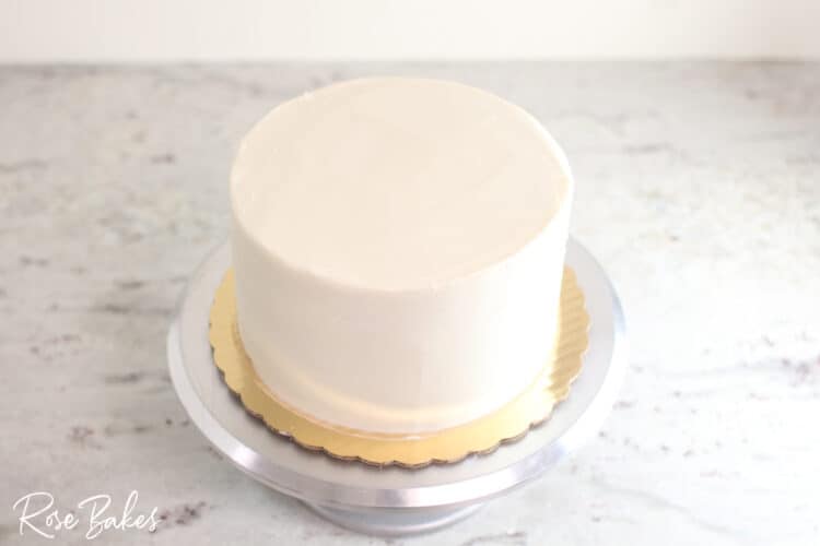 bottom tier of buttercream icing cake smoothed and on cake stand sharp edge