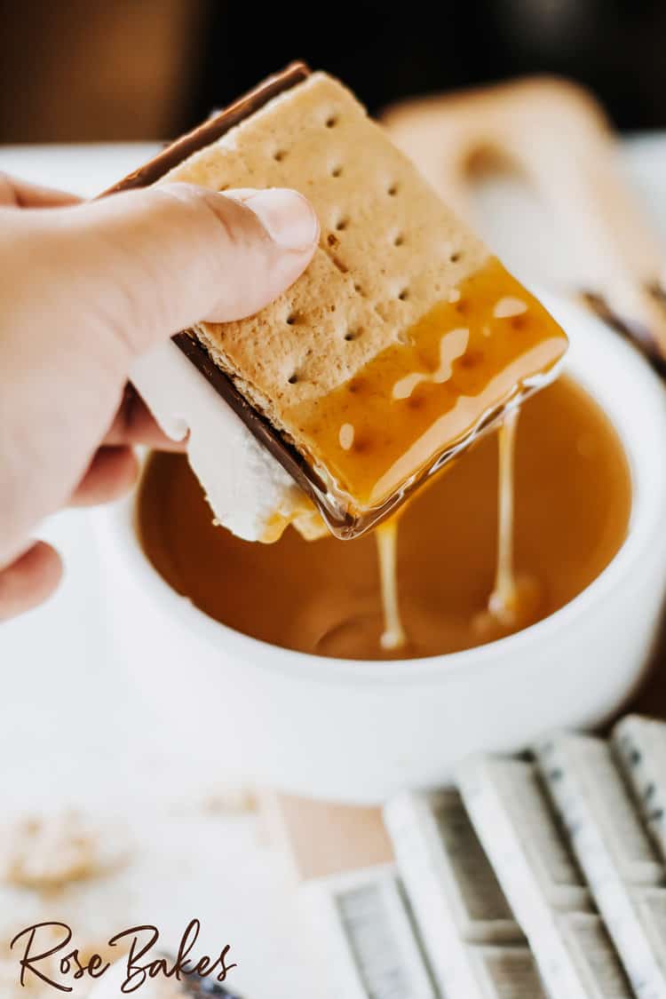 dipping a class s'mores bar in caramel sauce in a white bowl