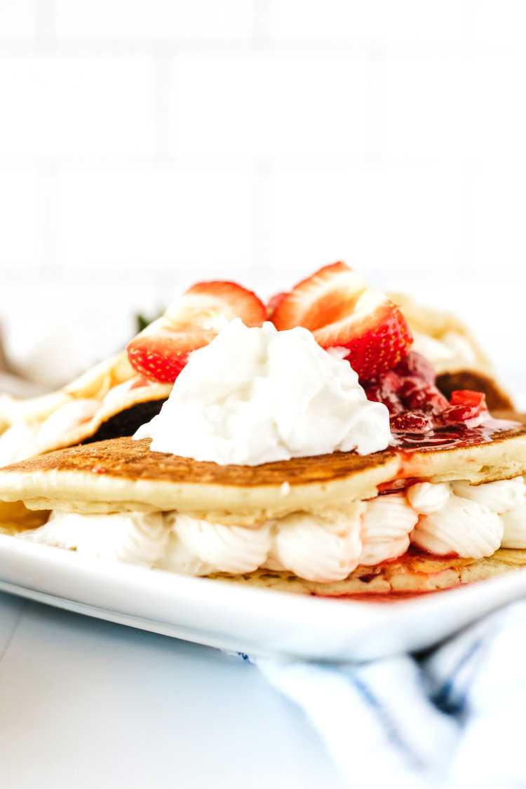 two buttermilk pancakes stuffed with no-bake cheesecake filling folded like tacos on a white plate with fresh strawberries and strawberry syrup on top - strawberry cheesecake stuffed pancakes