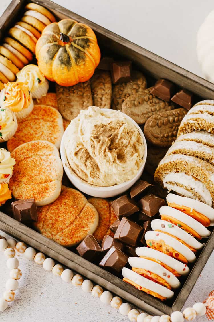 wooden tray filled with pumpkin cream cheese dip, cookies, candies, and fall cupcakes