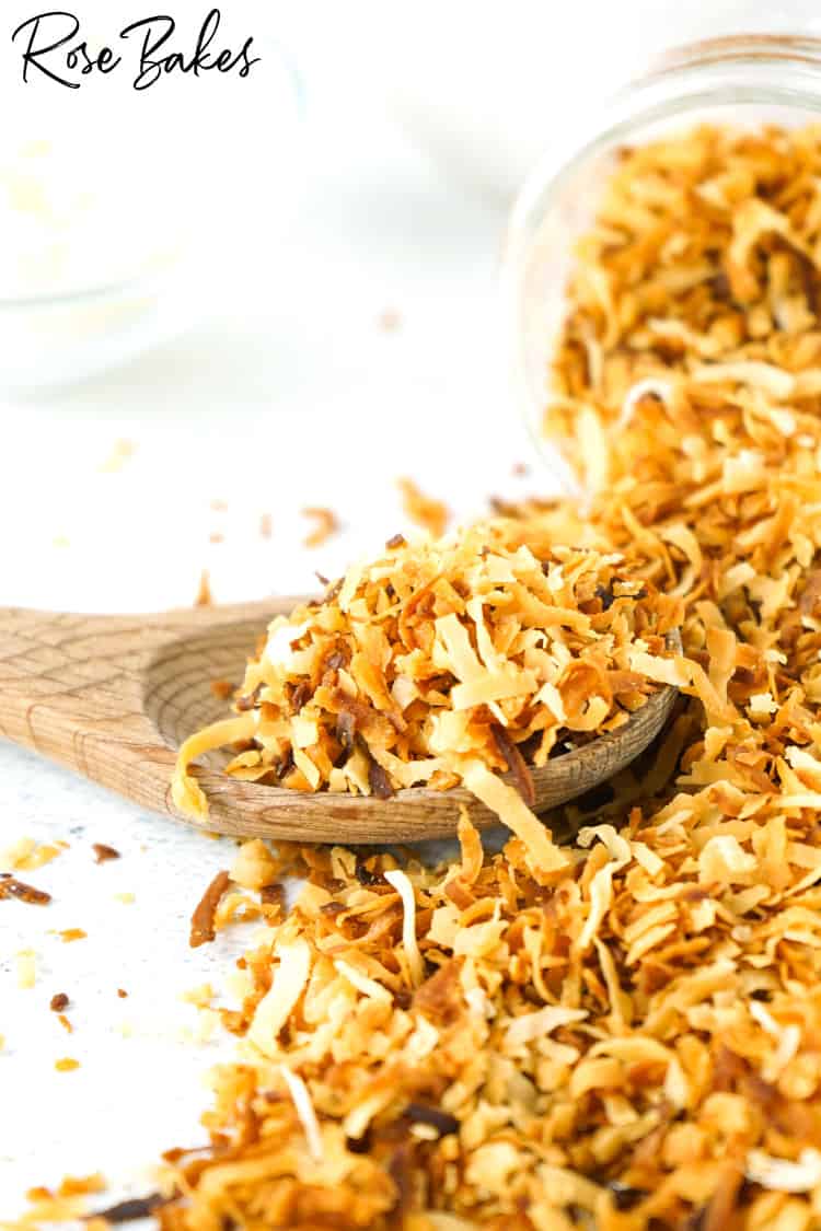 Toasted coconut spilling out of a jar and onto a wooden spoon.