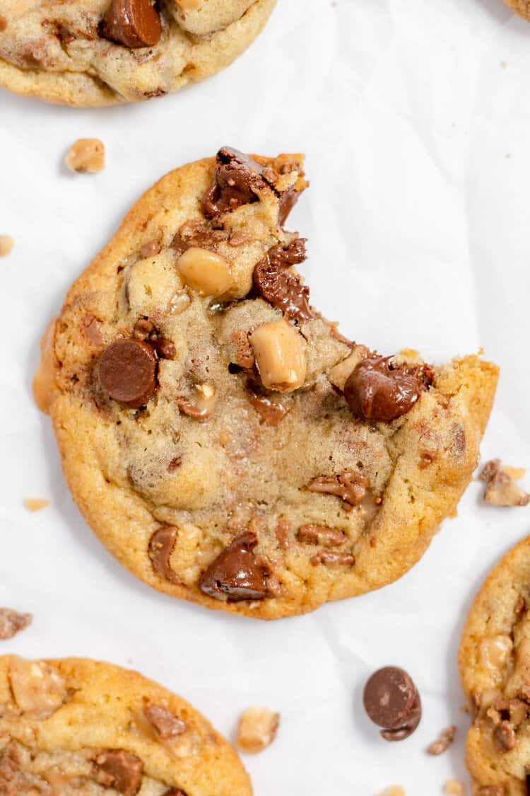 Toffee Chocolate Chip Cookies on parchment paper with a bite missing