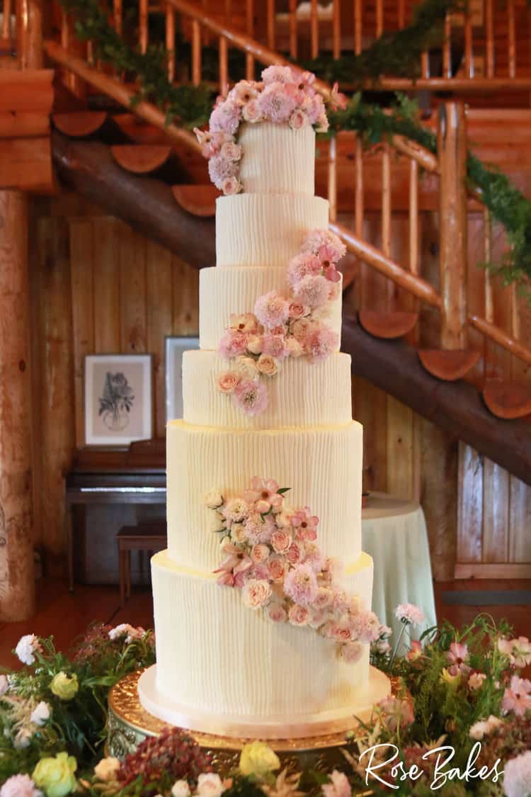 Vertical Lines Buttercream Luxury Wedding Cake on a table filled with fresh flowers that are pink and white
