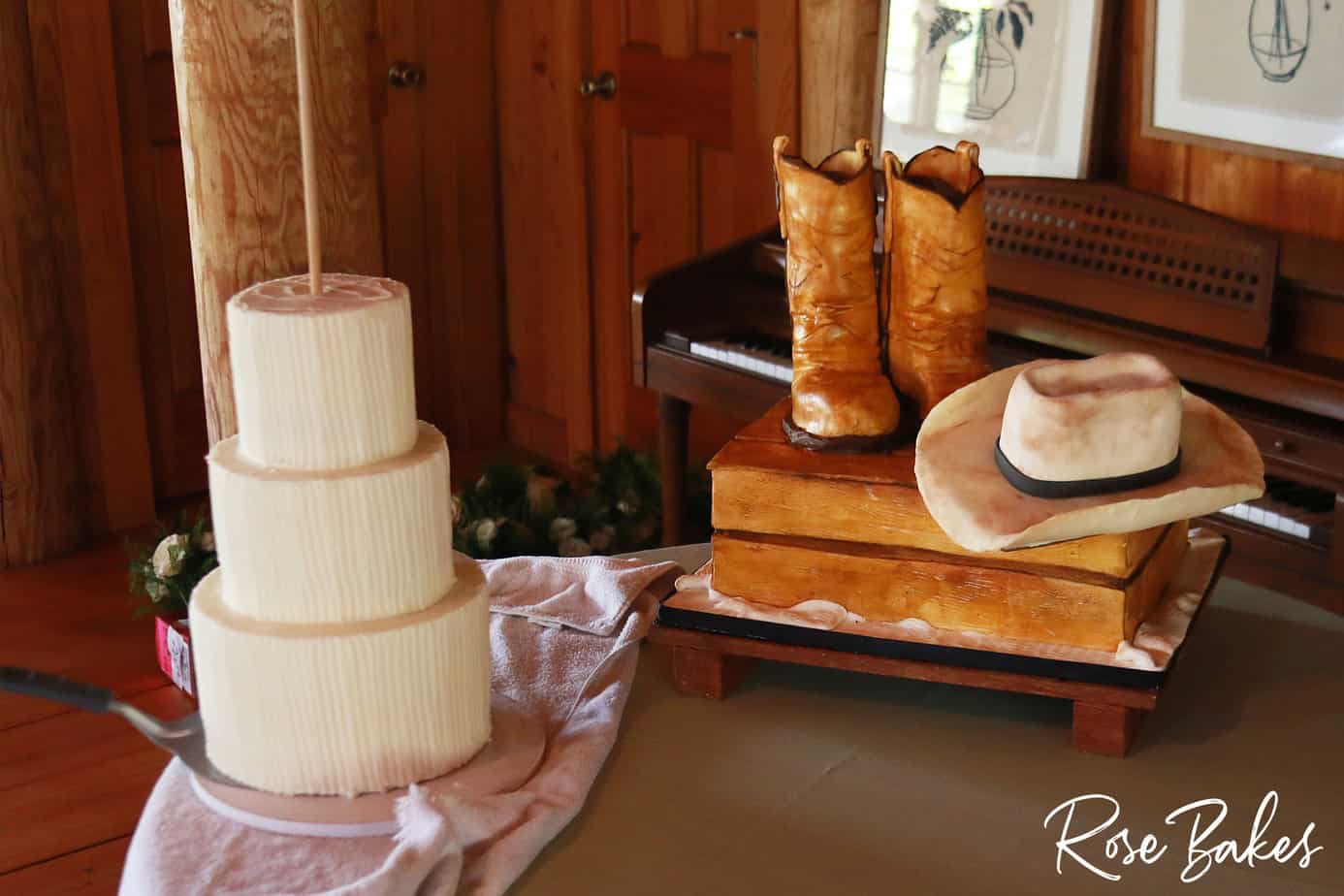 three tiers of wedding cake with vertical lined ribbed buttercream plus a a boots and hat groom's cake on a table