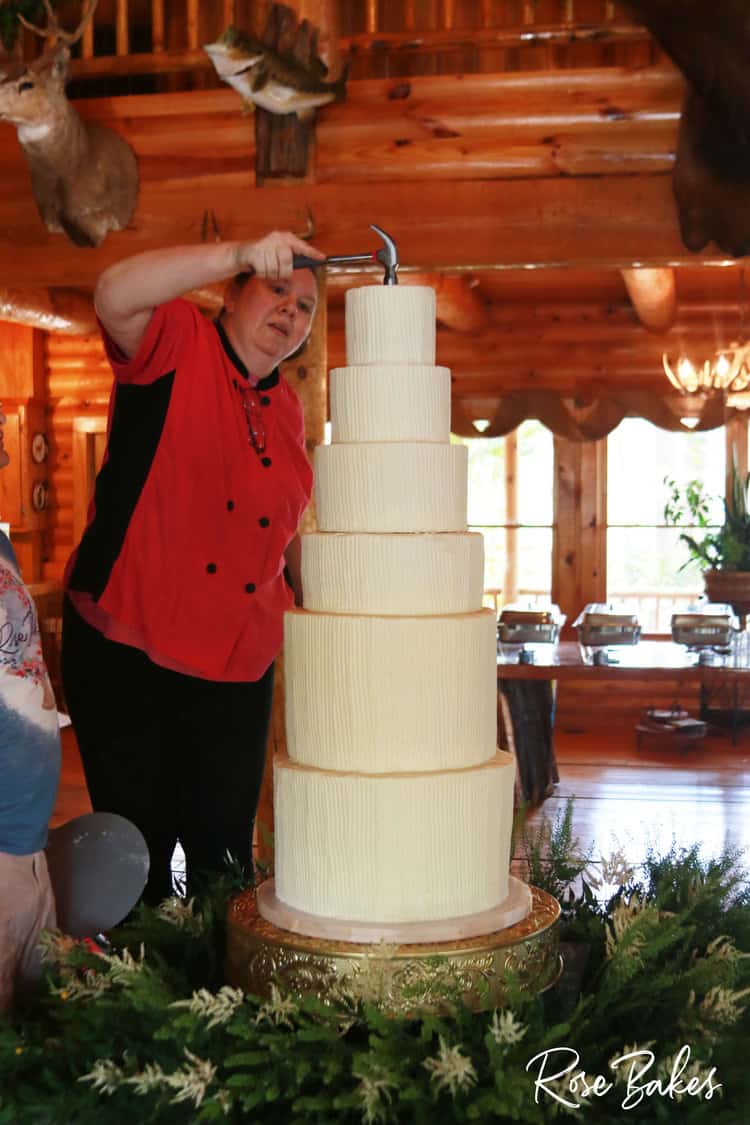 woman hammering a dowel into the top of a 6 tier wedding cake
