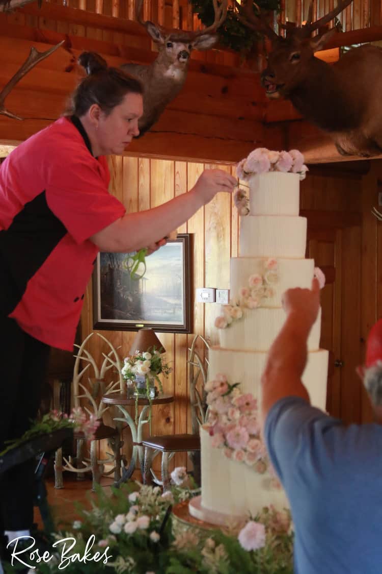 Rose standing on a stool adding flowers to a tall wedding cake