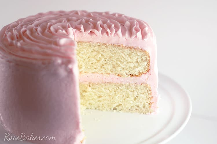 White Almond Sour Cream Cake filled and frosted with light pink frosting with a big slice taken out showing the inside of the cake.