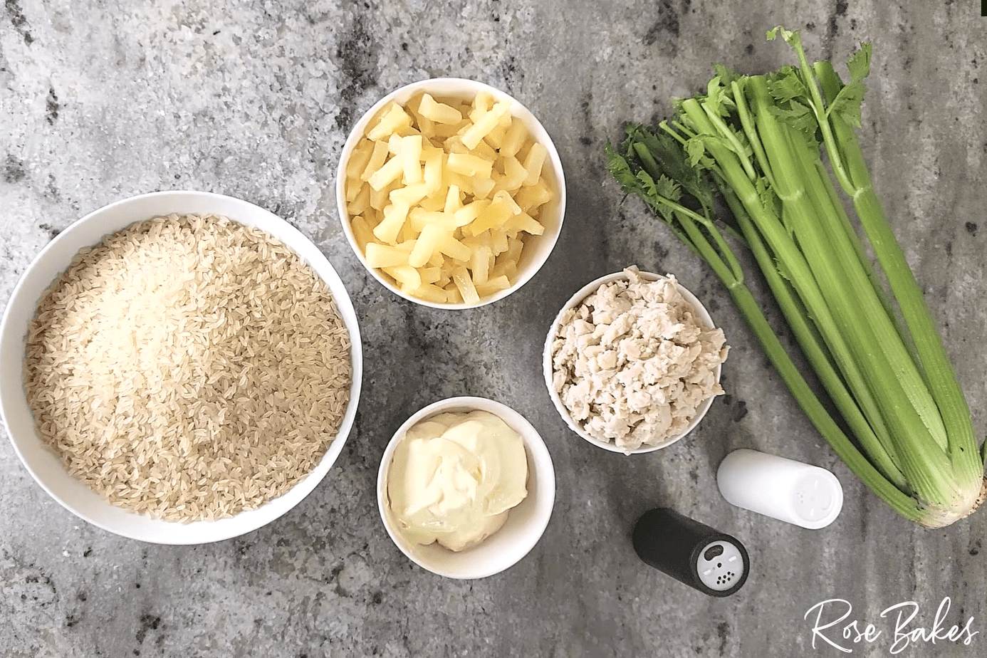 Bowls of rice, pineapple, mayo, chicken, salt and pepper shakers, and  stalk of celery